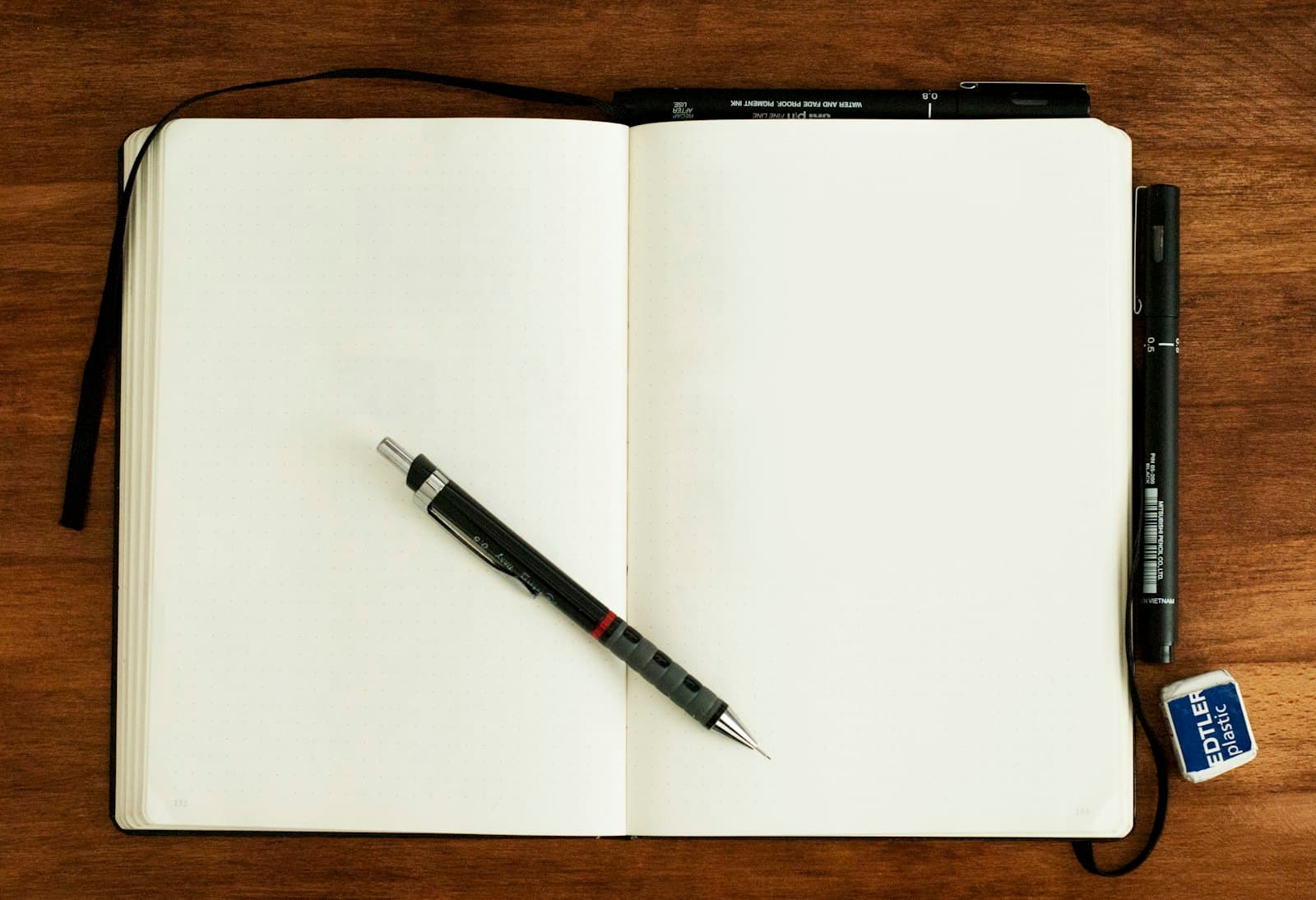 An open blank notebook with pens on a wooden desk